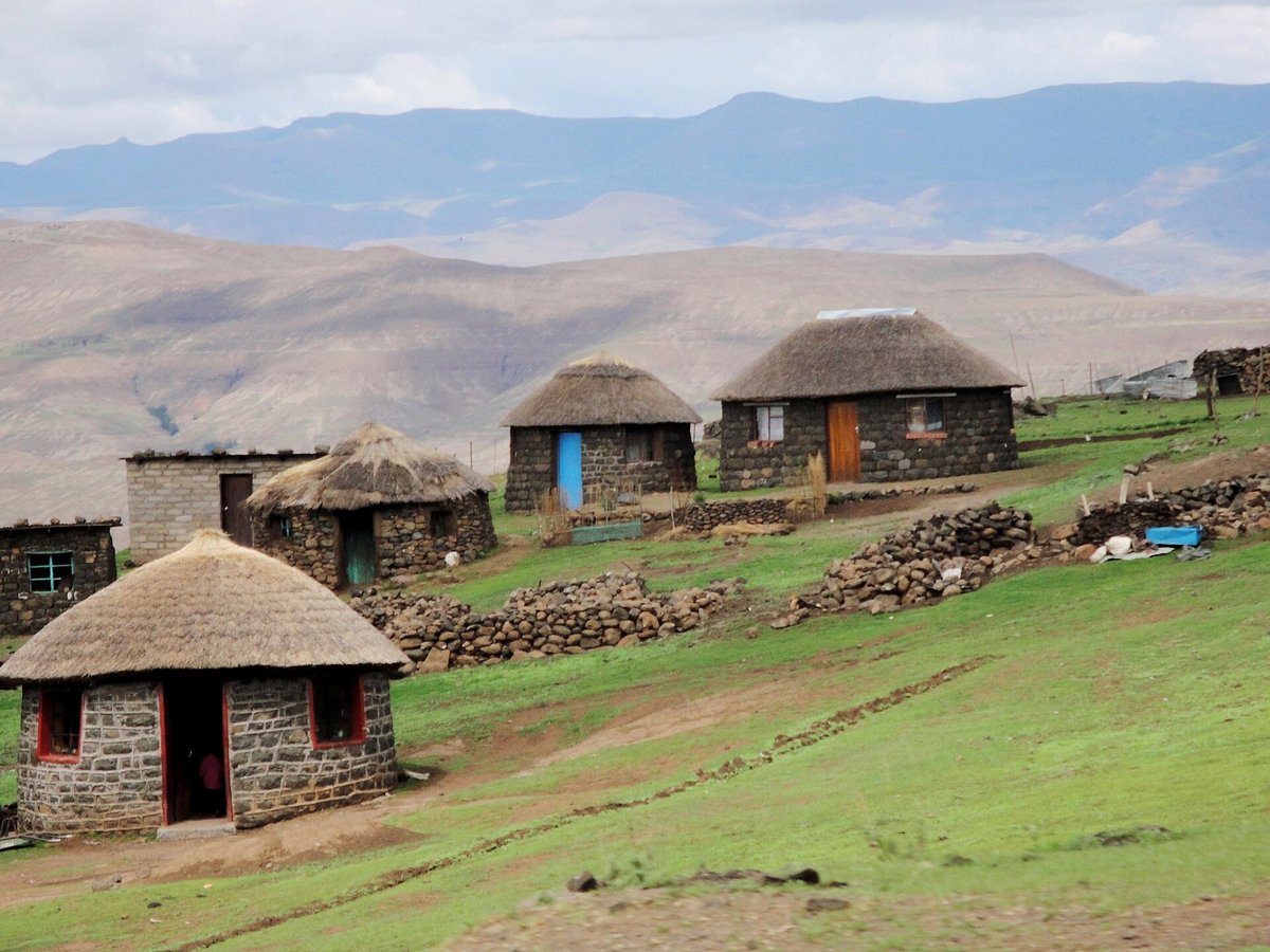 Village de montagne au Lesotho, maisons rondes en pierre à toit de chaume sur une pente herbeuse