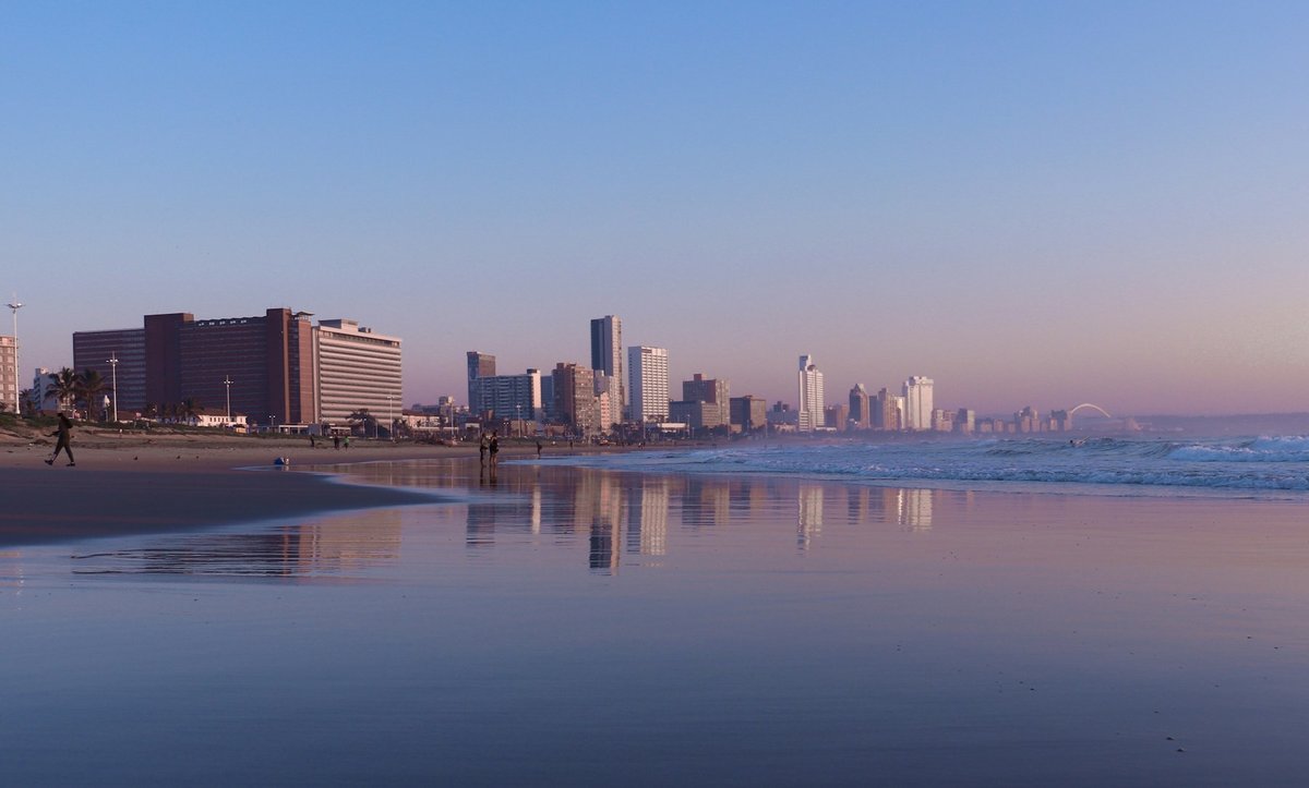 Plage de Durban au crépuscule, immeubles du front de mer reflétés sur le sable mouillé